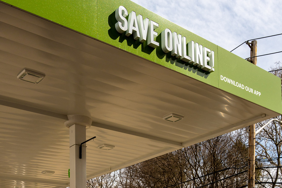 Gas station with a green banner with white signage stating "SAVE ONLINE!". A smaller text to the right of the sign says "download our app".